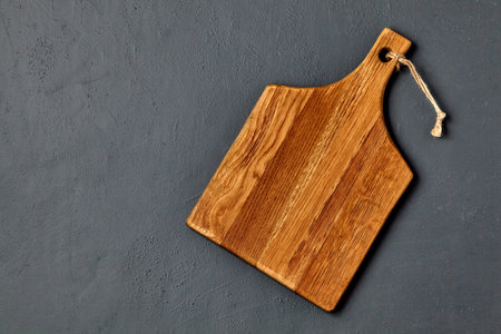 Brown wooden cutting board on a dark concrete table. Template for laying out dishes