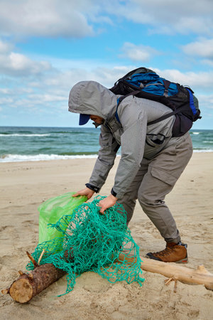 Male volunteer in windy weather collects garbage thrown by a storm on a sandy beach