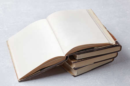Open vintage book with blank pages lies on a stack of old shabby books in a dust jacket on a gray...