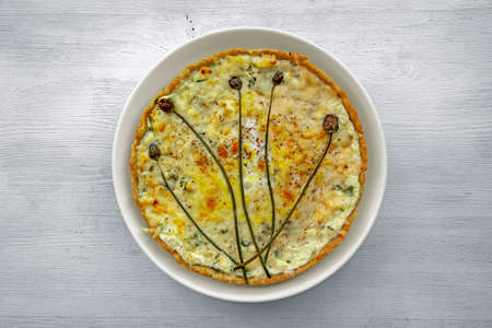 Open Laurent tart with meat and vegetables topped with creamy cheese filling on a white wooden tableの写真素材