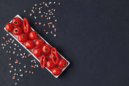 Fresh washed cherry tomatoes and paprika slices on a white oblong dish with pink salt on a black...