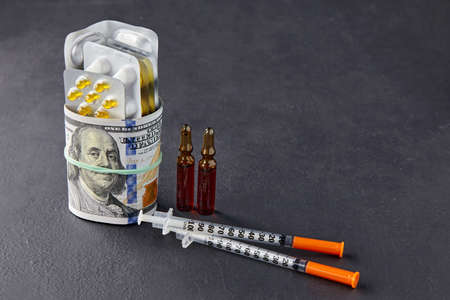 Pills, ampoules and syringes are wrapped in dollar bills, fastened with an elastic band on a black...