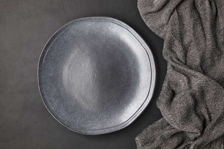 Dark empty handmade ceramic plate and kitchen towel on a black concrete table. Food display menu...