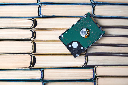 Computer hard drive on the background of a stack of old paper books. Comparison of the volumes of...