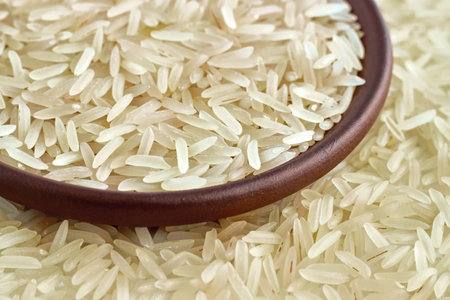 Healthy basmati rice in a clay ceramic bowl close-up against the background of scattered grains of rice.の写真素材