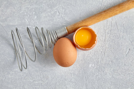 Two beige chicken eggs and a rare beater for beating. Cooking ingredients isolated on white background. top view with copy spaceの写真素材
