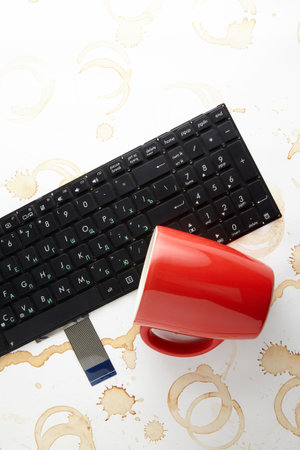 Keyboard with Cyrillic characters filled with drink. A red cup of coffee is knocked over on a computer keyboardの写真素材