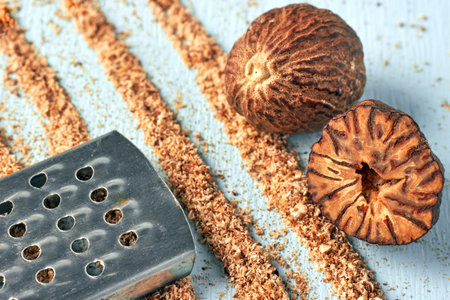 Two nutmegs and a metal grater against the background of grated nutmeg powder tracks on a blue wooden table.の写真素材