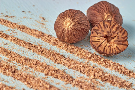 A group of nutmeg nuts and paths with gratified nutmeg powder on a light blue table background.