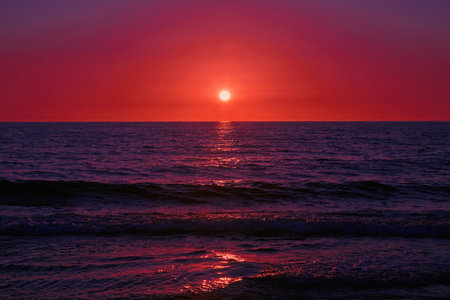 The blood red sun sets on the blue ocean. Dramatic sunset on the sea.