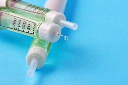 Insulin syringe pen with a drop of insulin at the end of the needle on a blue background