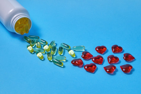 Omega 3 polyunsaturated fatty acids and red hearts pour out from a white plastic jar on a blue...