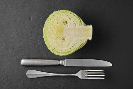 White cabbage in a cut, fork and knife on a black stone tabletop.の写真素材
