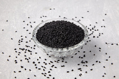 Black cumin (Nigella sativa) in a crystal bowl scattered on a grey concrete table.
