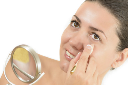 Young woman using concealer looking in the mirrorの写真素材