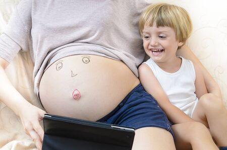 Child smiling near his mother tummy looking to tablet pc