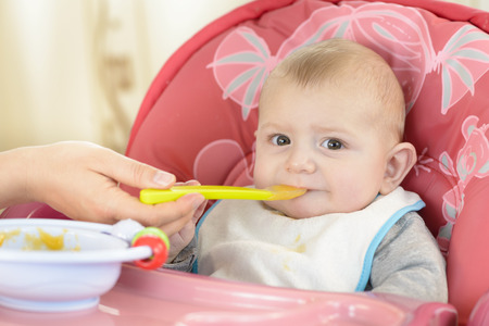 Baby boy eating in a high chair at homeの写真素材