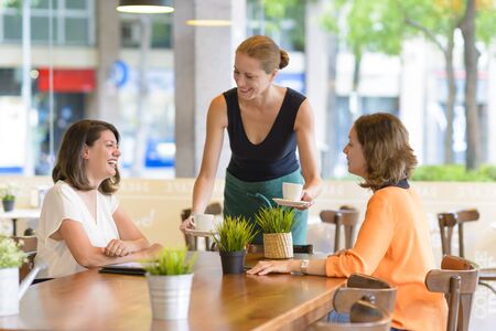 Waitress serving two happy women in a restaurantの写真素材