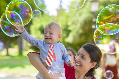 Cute baby and his mother catching soap bubbles in a summer dayの写真素材