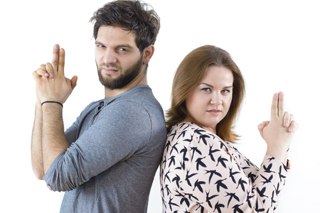 Funny couple having tough expression, holding imaginary guns standing back to backの写真素材