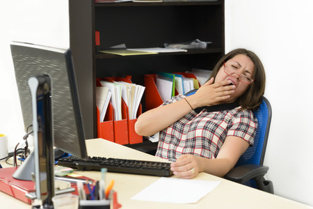 Sleepy woman working at office, typing, using the computerの写真素材