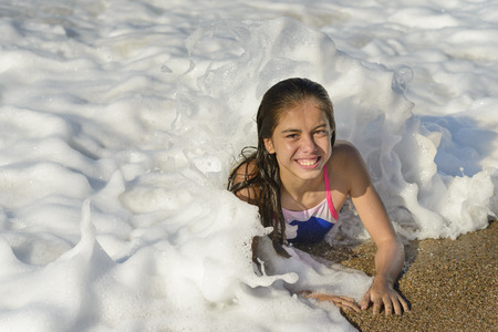 Happy girl laying down, relaxing on beach, waves and foam around, in a sunny summer dayの写真素材