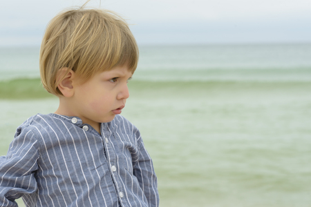 Cute upset boy looking serious on seasideの写真素材
