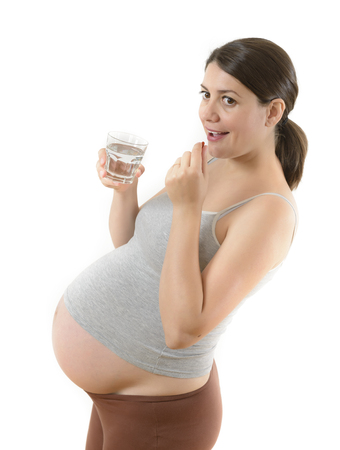 Beautiful smiling pregnant woman taking a pill isolated on whiteの写真素材