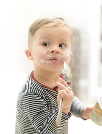 Little boy eating yogurt with strong appetite, having a funny messy face