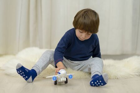 Cute little lonely boy playing with a toy plane sitting down on fur at homeの写真素材