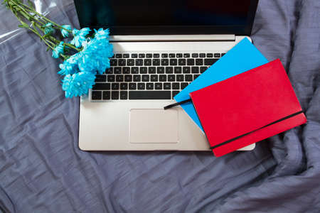 Work space at home, keyboard top view, female hand close up, notebook, work space on bed top view, flowers, colour backgroundの写真素材