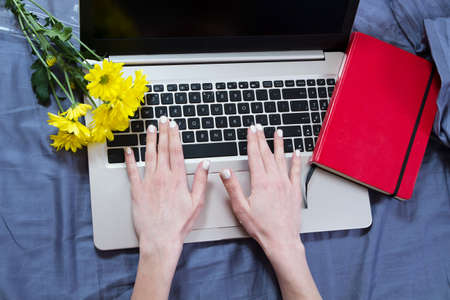 Work space at home, keyboard top view, female hand close up, notebook, work space on bed top view, flowers, colour backgroundの写真素材