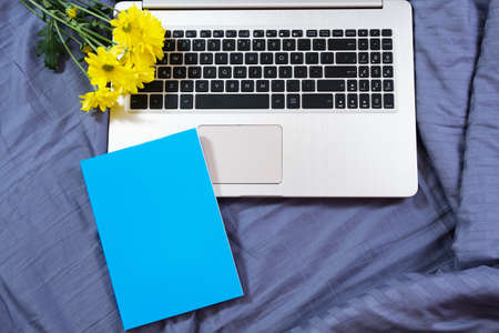 Blue notepad mock up on laptop and yellow flowers background close upの写真素材