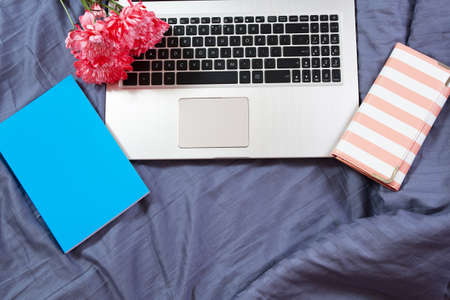 Work space at home, keyboard top view, female hand close up, notebook, work space on bed top view, flowers, colour backgroundの写真素材