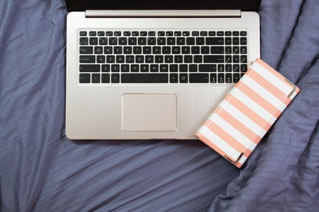 flat lay image of workplace background, laptop and clatch on bed close upの写真素材