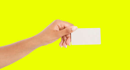 afro american hand showing paper card isolated on yellow background, arm hold businesscardの写真素材