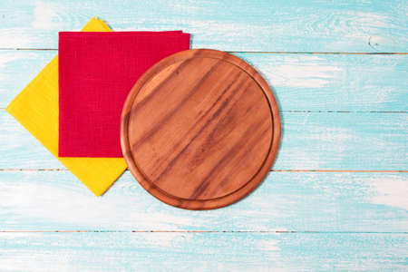 top view of empty wood pizza board and colored napkin tablecloth on wooden table, copy space