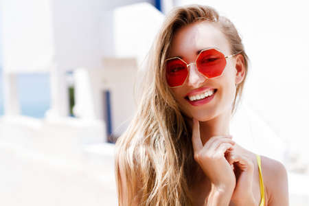 Very beautiful white woman in stylish red sunglasses posing on a sea background of a hotel of the sea and tropicsの写真素材