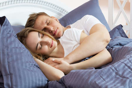 Young cute couple sleeping together in bedの写真素材