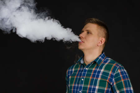 white Man in chekered shirt vaping and releases a cloud of vapor Selective focus