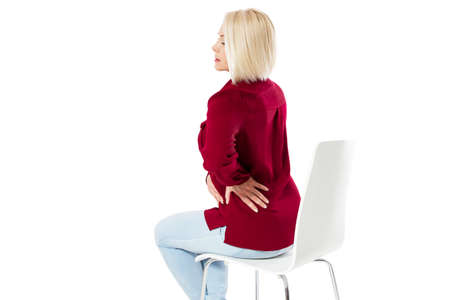 Woman female back ache, back pain - middle age woman sitting on chair and massaging back painの写真素材