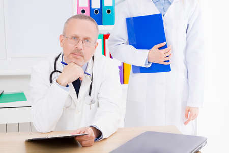 doctor posing in office with medical staff, he is wearing a stethoscope. quality medicine concept....