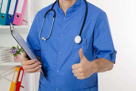 Portrait of cheerful male doctor in hospital takes notes. Surgeon with stethoscope on white...