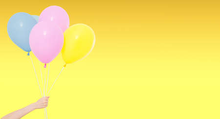 hand hold colored balloons isolated on yellow background, holiday and funの写真素材