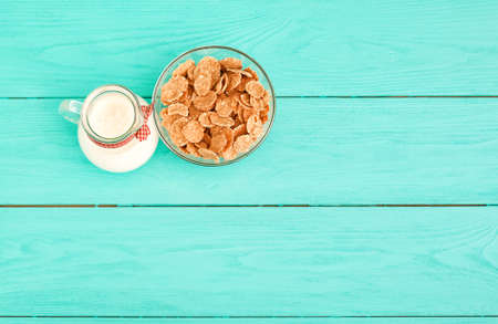 Oat flakes and jug of milk on blue wooden background. top view