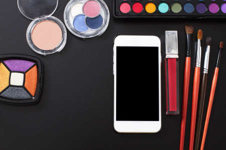Cosmetic products and make up accessories on black background. Smartphone with blank screen. Top view and copy space. summer colorsの写真素材