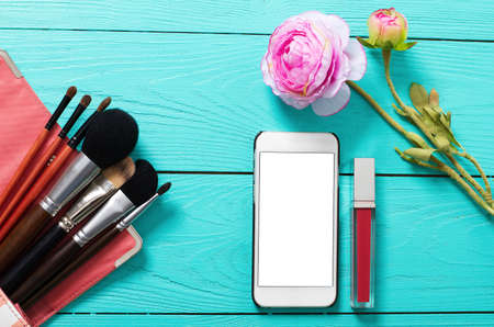 Frame of cosmetic products and blank mobile screen on blue wooden background. Top view and copy space. decorative flowerの写真素材