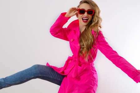Close up happy girl in red sunglasses and pink coat isolated on white background. excited, shock and surprised young woman, trendy outfit. Fashion and shopping concept. long wavy hair. selective focusの写真素材