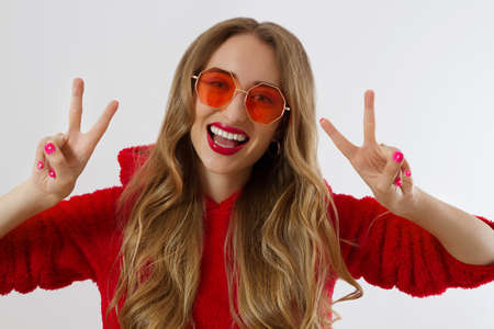 Young woman in red hoodie sweatshirt isolated on white background. Fashion and style concept. peace sign gesture. Happy beautiful girl in red sunglasses. Make-up and beauty. Glamor model. Kiss faceの写真素材