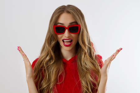Closeup excited screaming young woman. shock, shocked girl in red hoodie. Wow, surprised female. Fashion sweatshirt isolated on white background, face in red sunglasses. Beautiful, fashionable conceptの写真素材